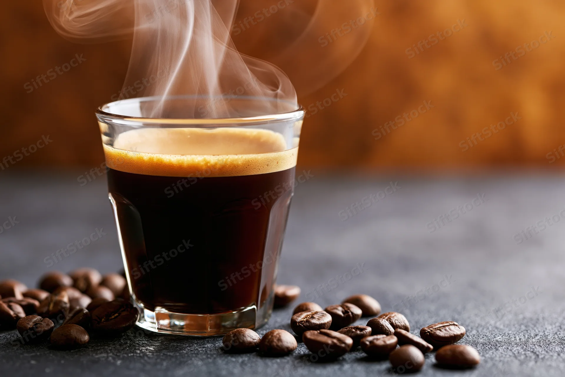 Steaming espresso in a glass cup surrounded by coffee beans on a dark surface