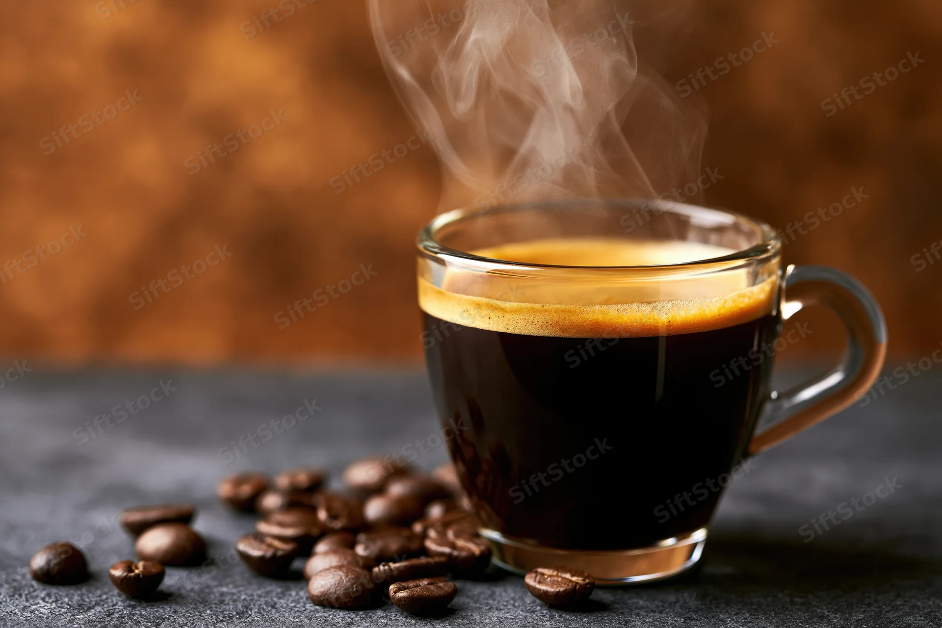 Steaming espresso in a glass cup with scattered coffee beans on a dark surface