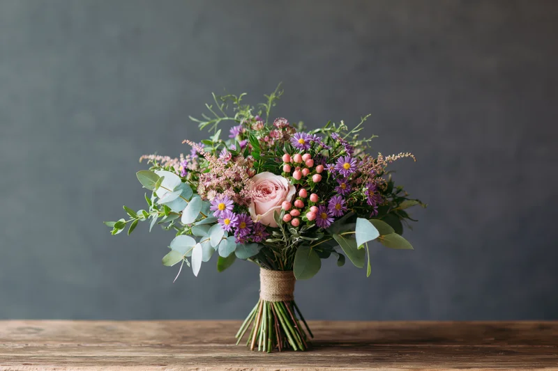 Hand-tied wildflower bouquet with roses and eucalyptus on a wooden table against a gray background