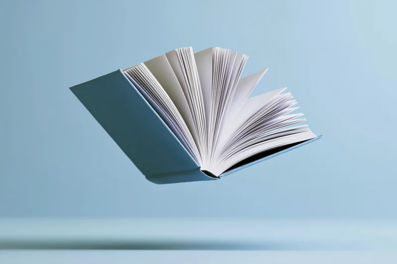 Open hardcover book floating midair with pages fanned against a blue background