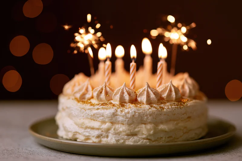 Layered cream birthday cake with lit striped candles and sparklers on a plate