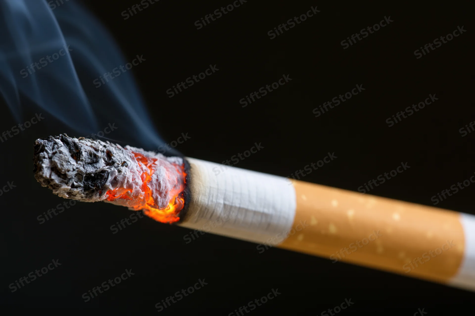 Lit cigarette burning with glowing ember and smoke against black background