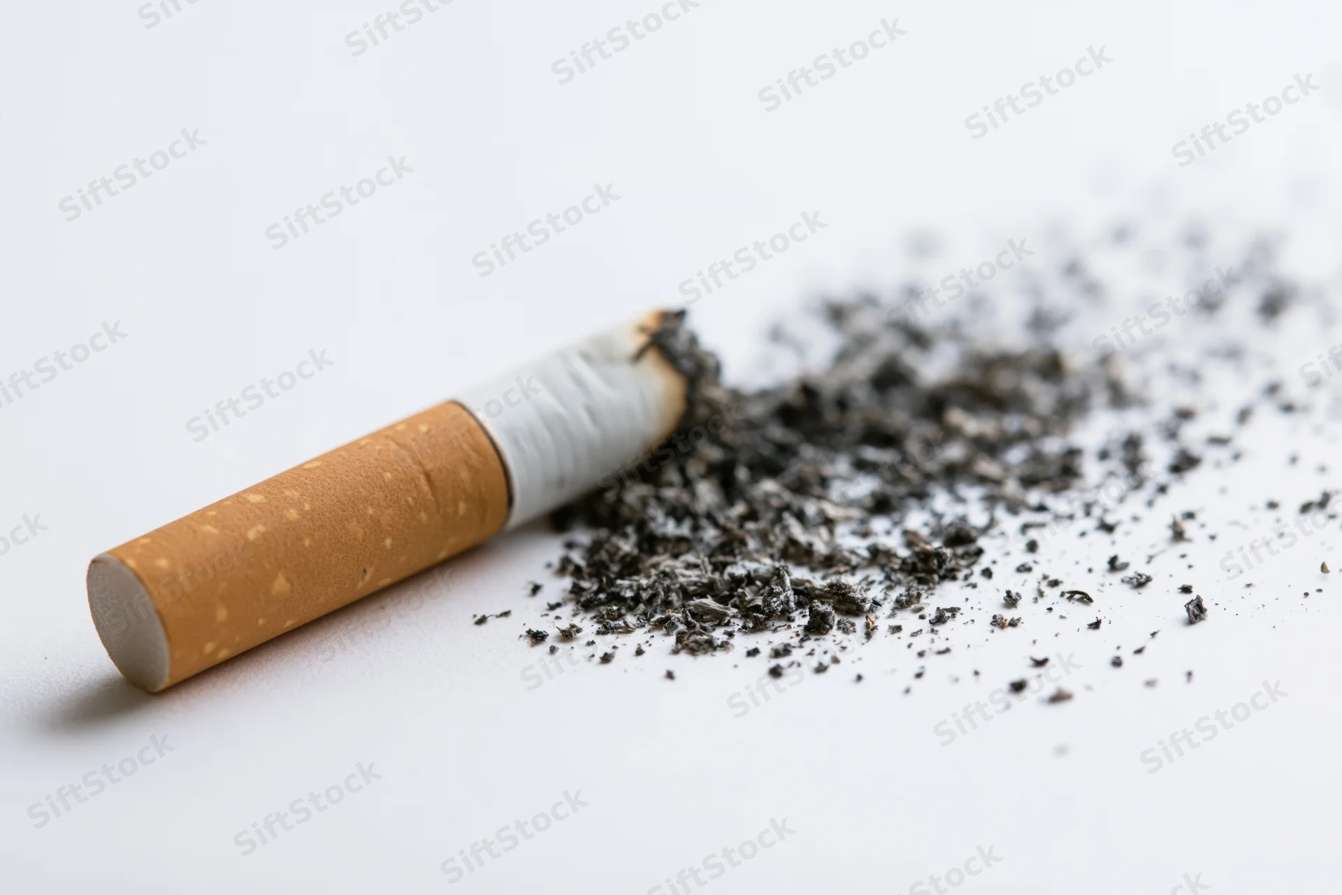 A cigarette with disintegrating ash lying on a white surface
