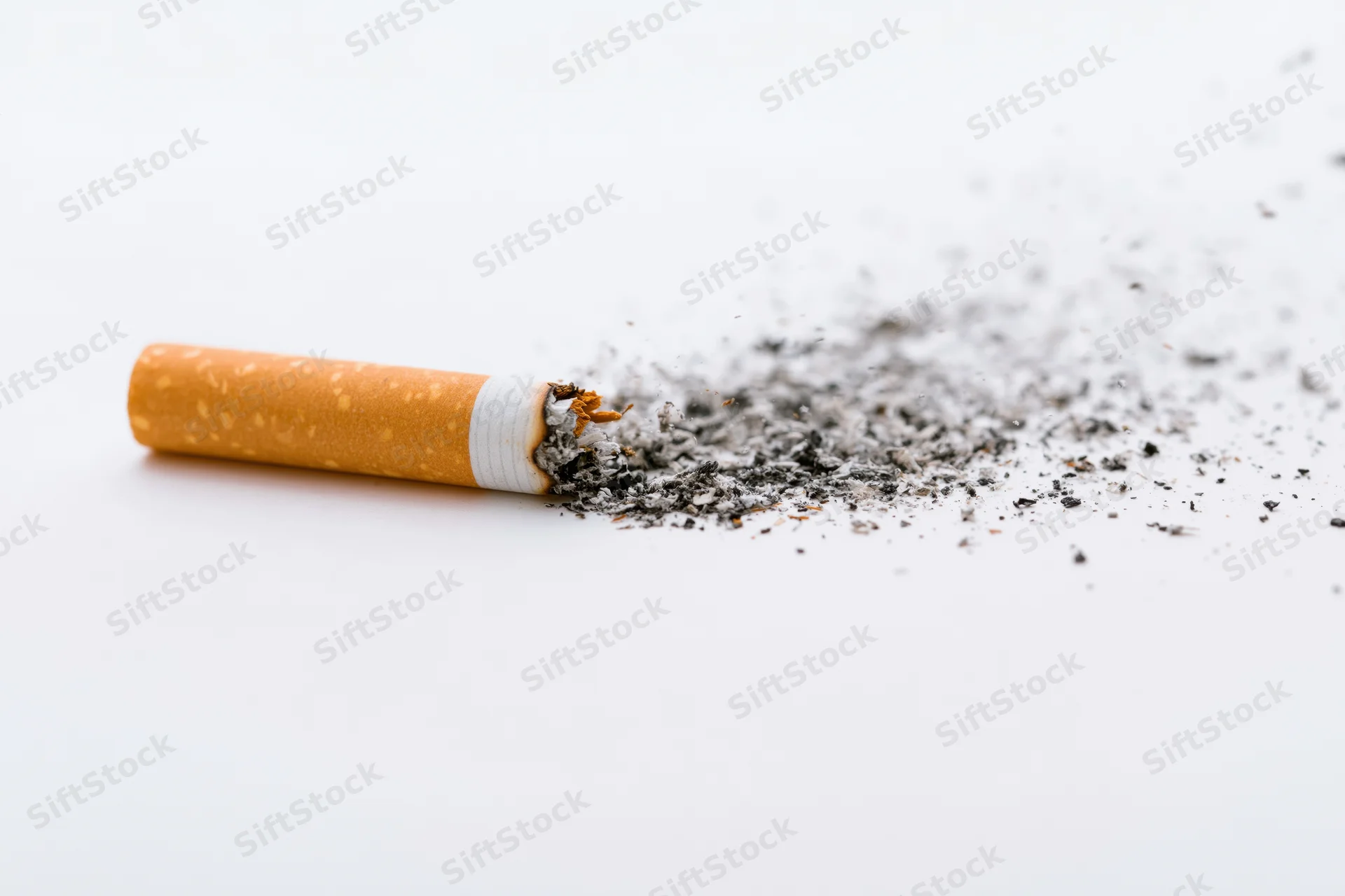 Cigarette with disintegrating ash lying horizontally on white surface
