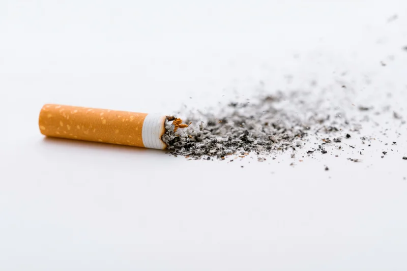 Cigarette with disintegrating ash lying horizontally on white surface