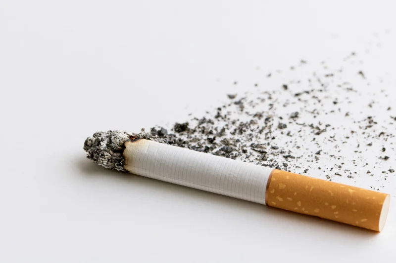 Lit cigarette lying horizontally with disintegrating ash on white surface