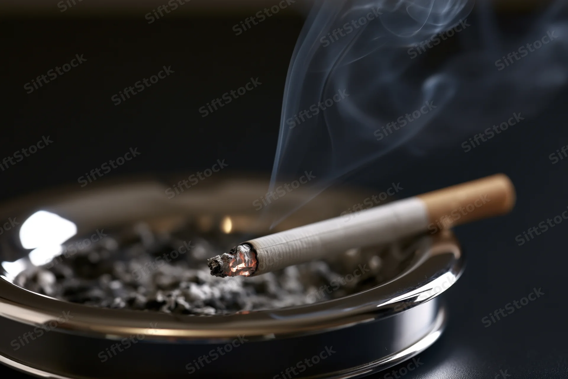 Lit cigarette resting on metal ashtray with rising smoke in dark indoor setting