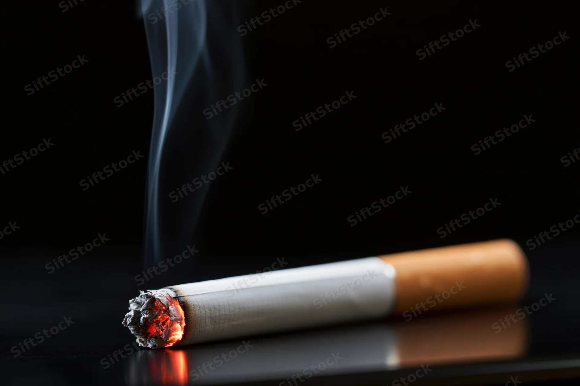 Lit cigarette burning with smoke rising on a dark reflective surface