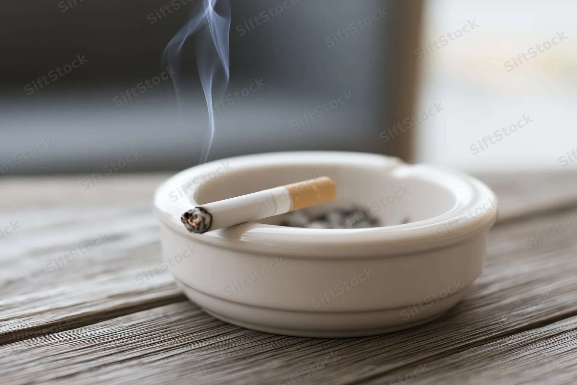 Lit cigarette resting in white ceramic ashtray on wooden table