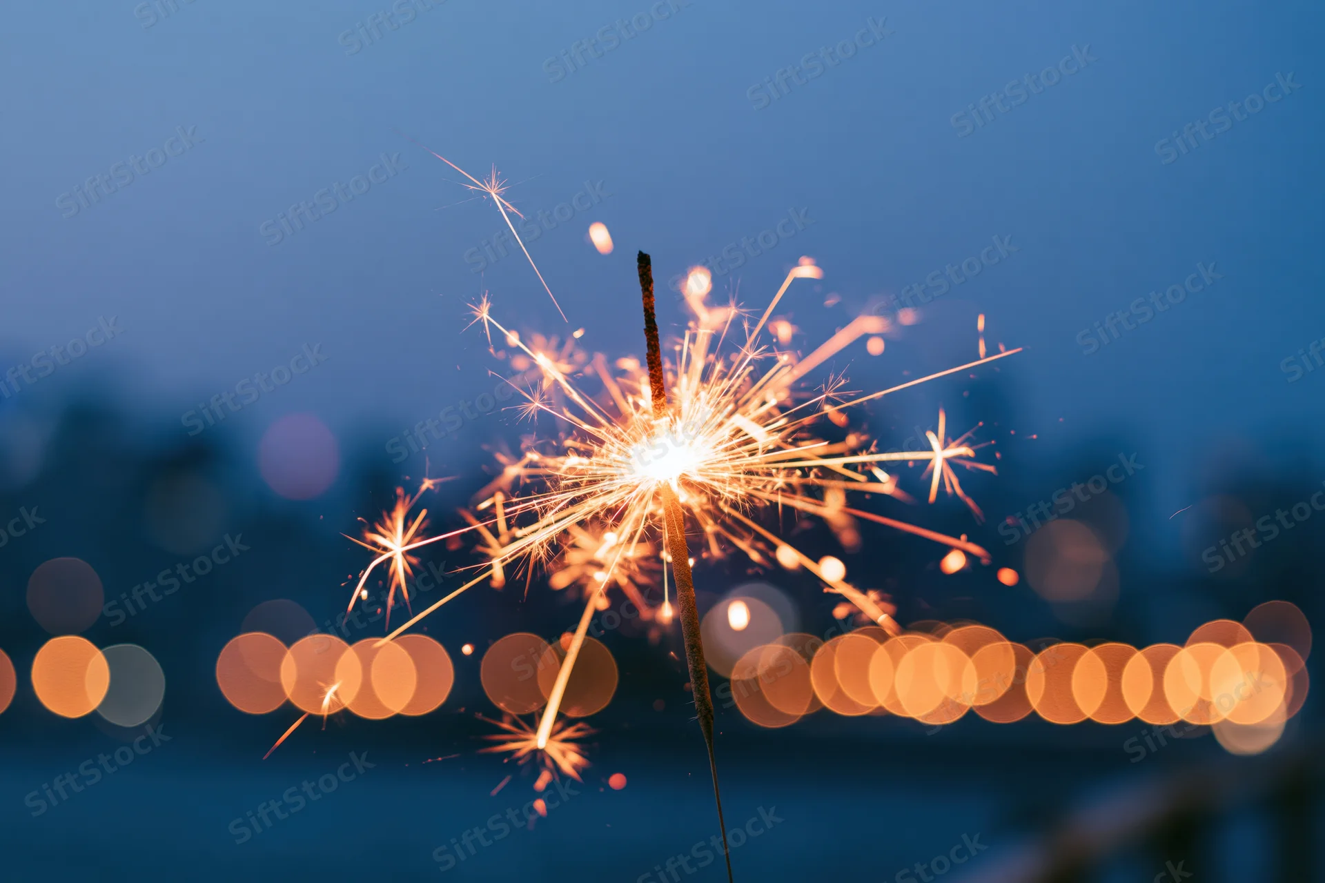 Lit sparkler glowing brightly against twilight cityscape with bokeh lights in background