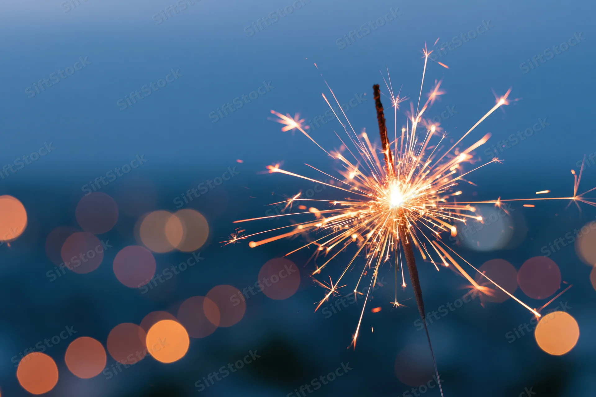Lit sparkler glowing brightly against twilight city lights with bokeh background