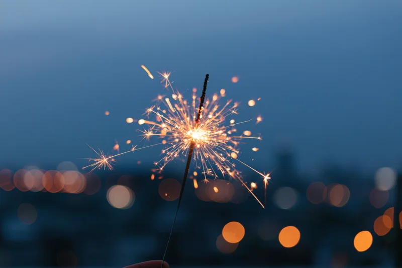 Hand holding lit sparkler against twilight city skyline with bokeh lights