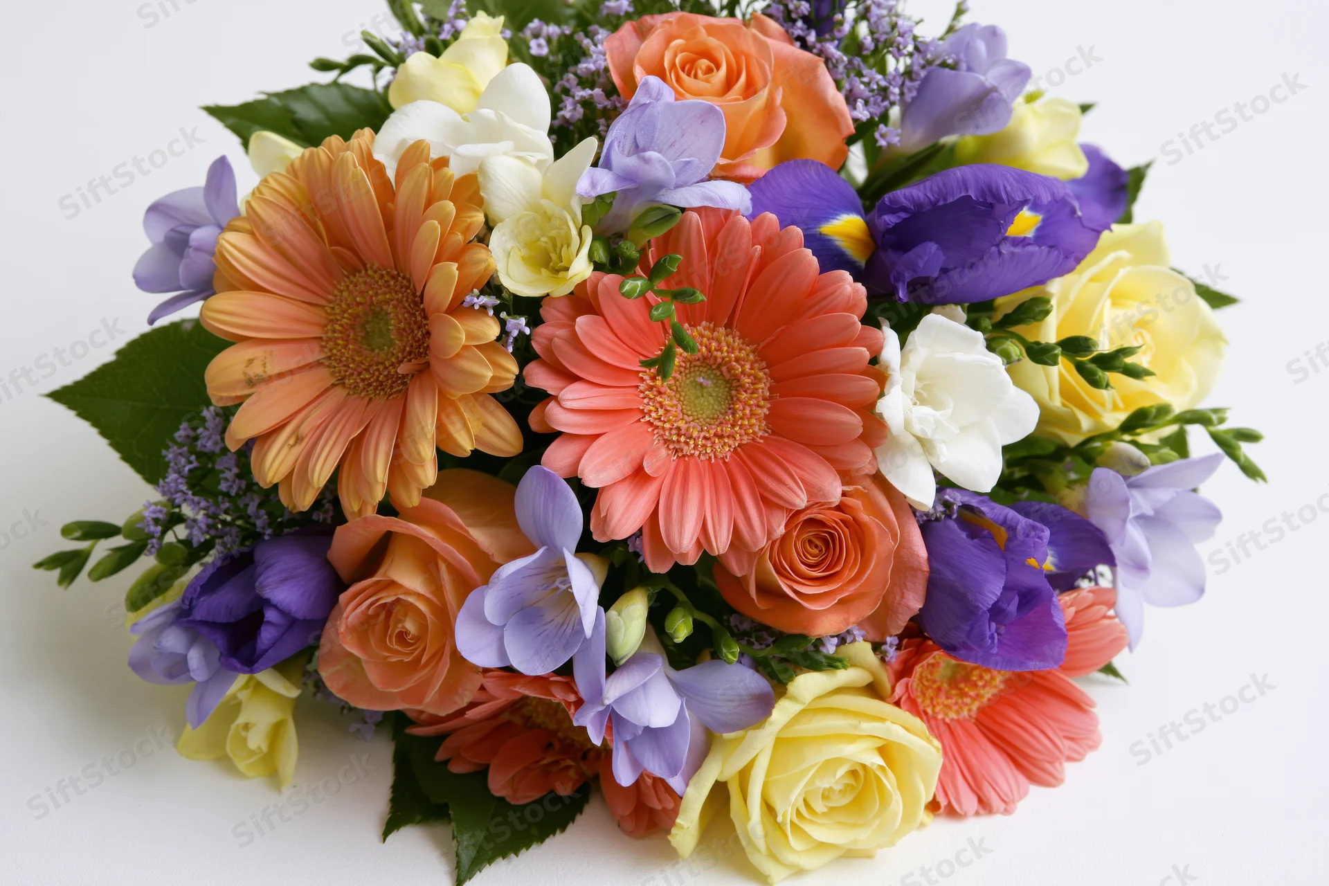 A dense mixed flower bouquet with gerbera daisies, roses, iris and freesia arranged on a white background