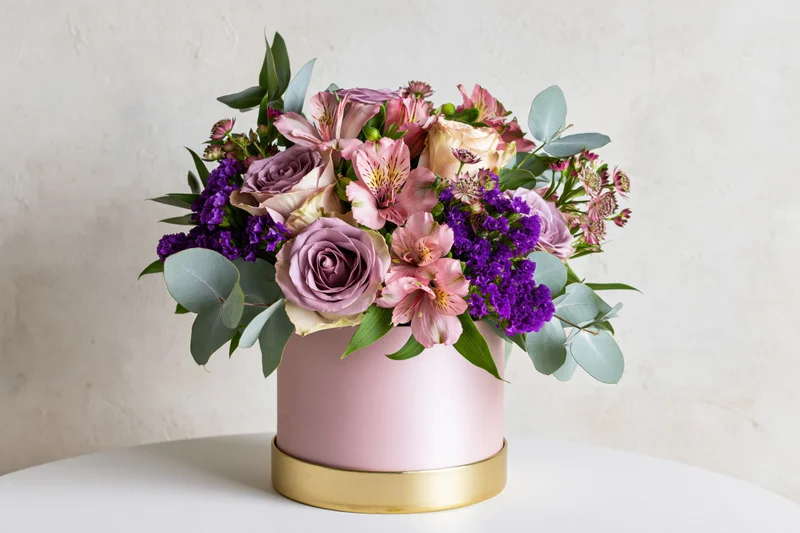 Lush mixed flower bouquet in pink cylindrical vase with gold rim on white table