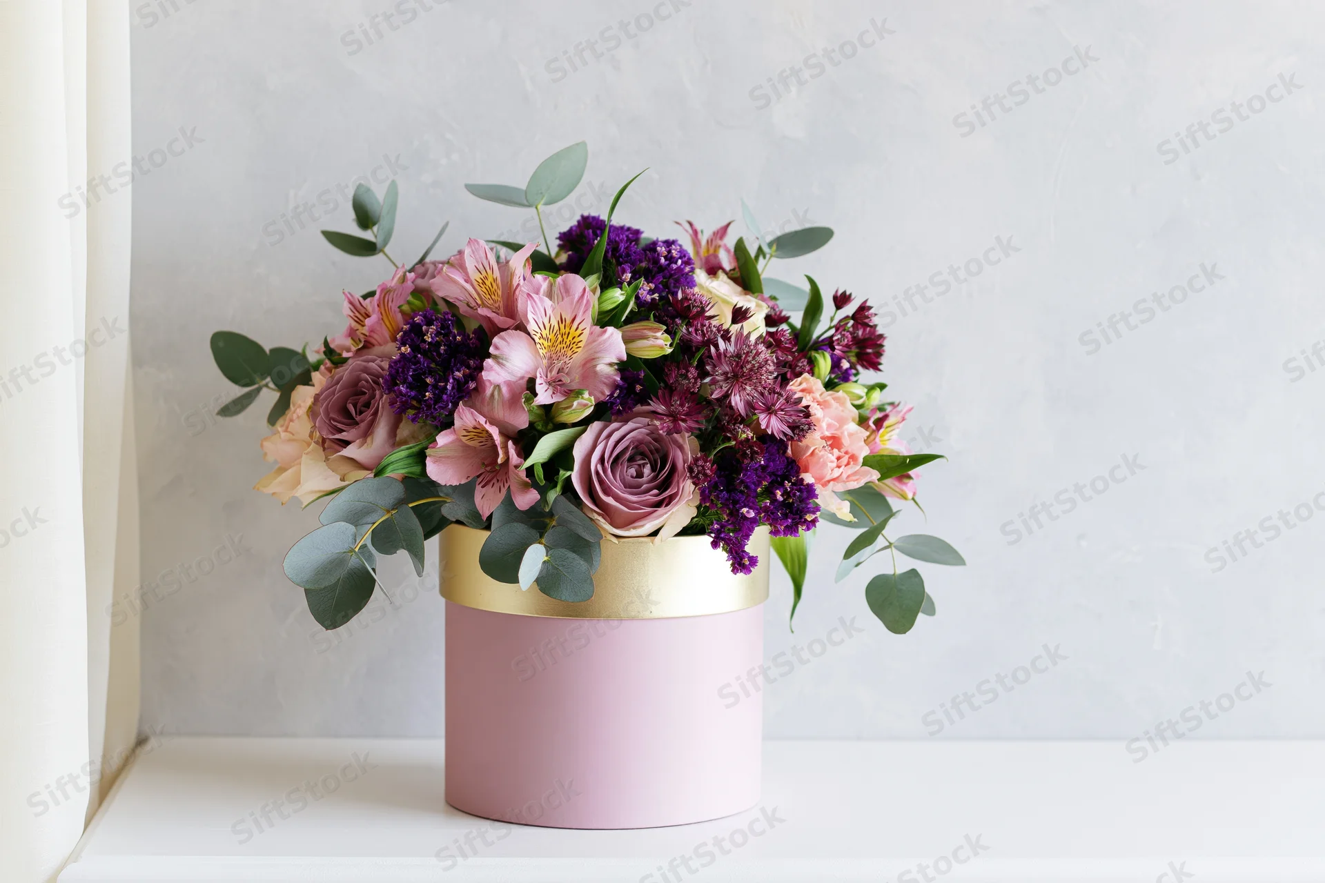 Lush mixed flower bouquet in pink cylindrical box on white surface