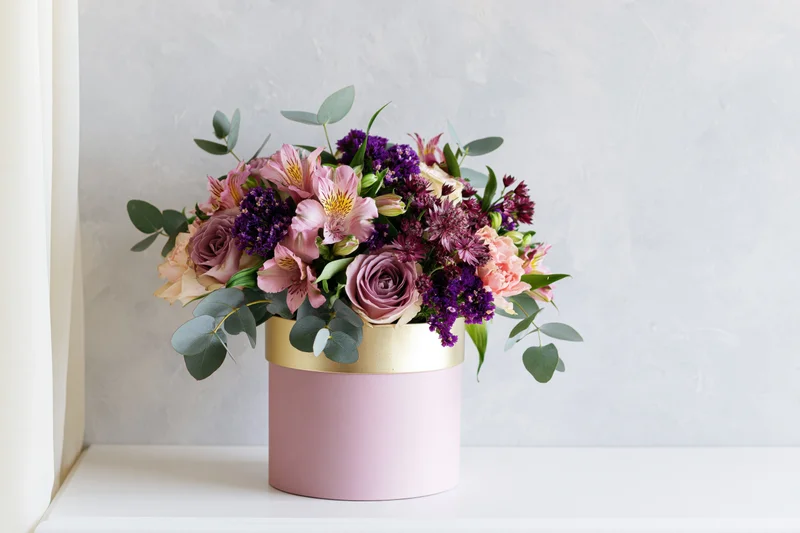 Lush mixed flower bouquet in pink cylindrical box on white surface