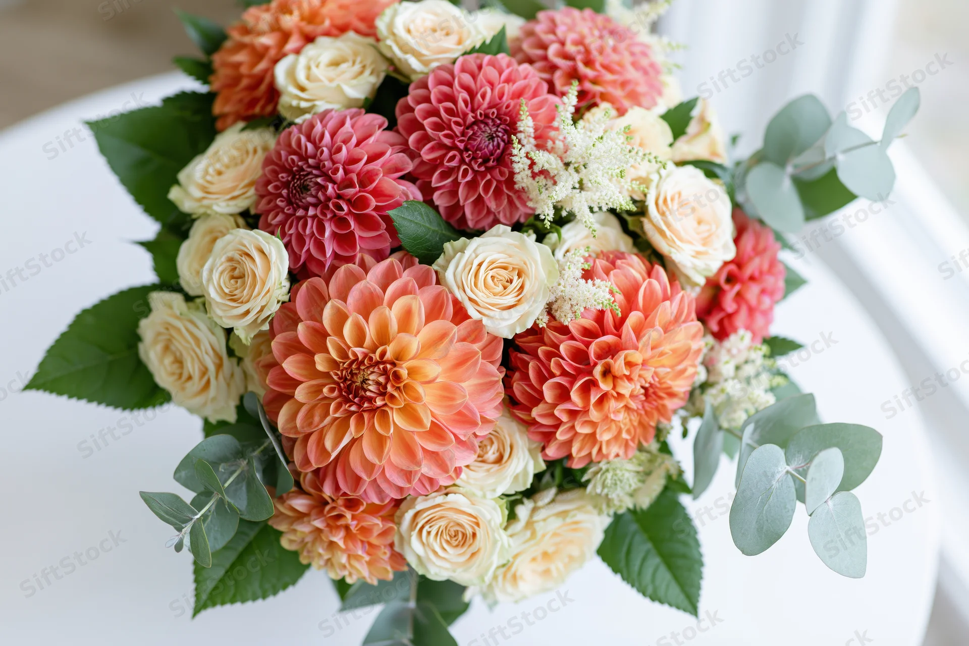 Lush mixed bouquet of dahlias, roses, and eucalyptus resting on a white surface