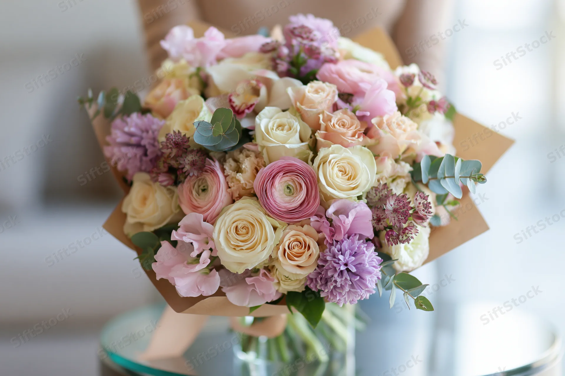 Lush mixed flower bouquet wrapped in kraft paper resting on a glass table