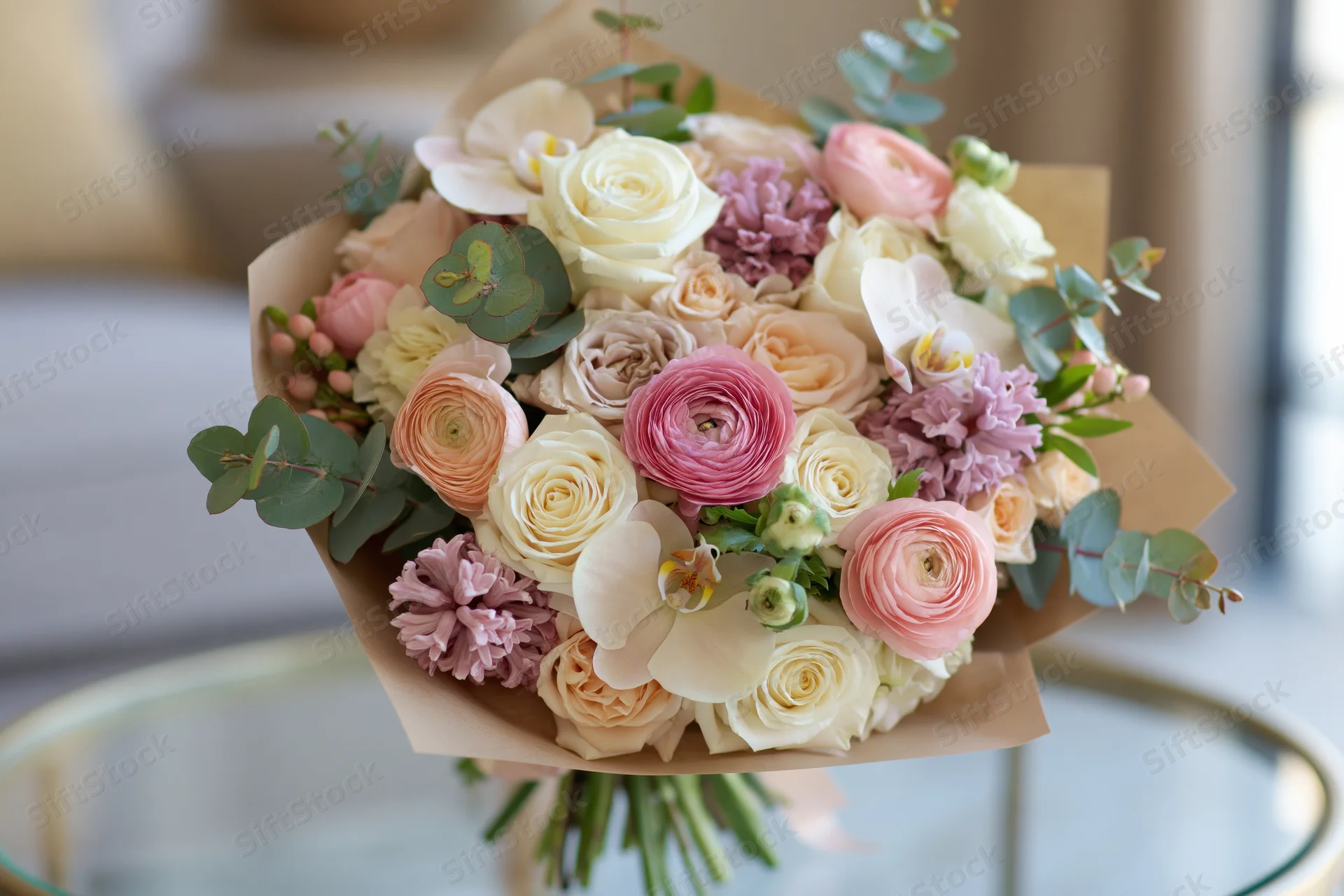 Lush mixed flower bouquet wrapped in kraft paper resting on glass table
