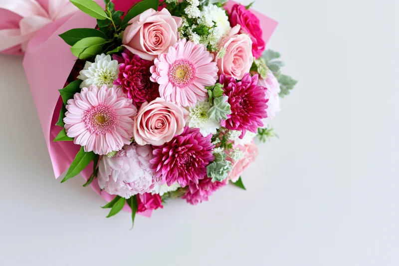 Mixed floral bouquet with pink roses, gerbera daisies and chrysanthemums wrapped in pink paper on white background