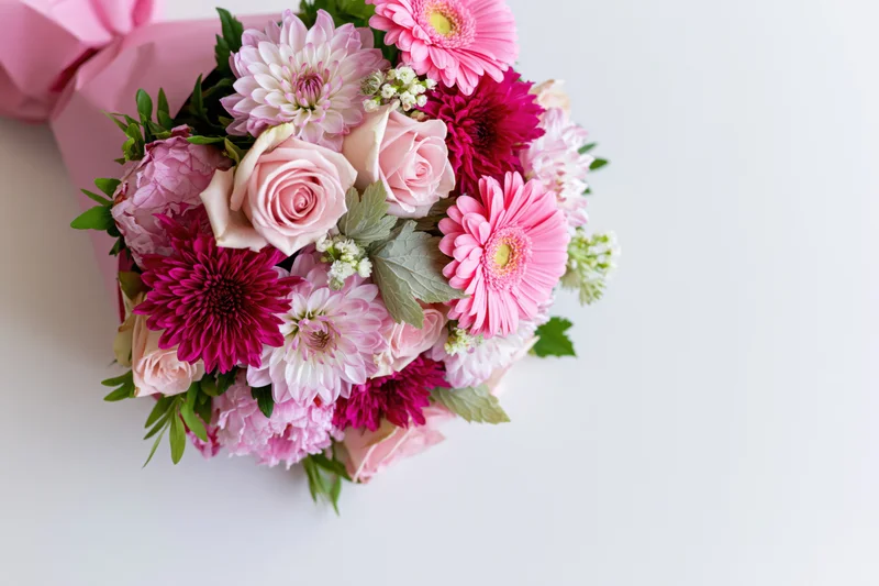 Pink floral bouquet with roses and gerbera daisies wrapped in paper on white surface