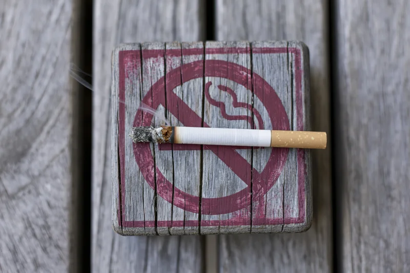 Lit cigarette resting on a no-smoking sign painted on weathered wood