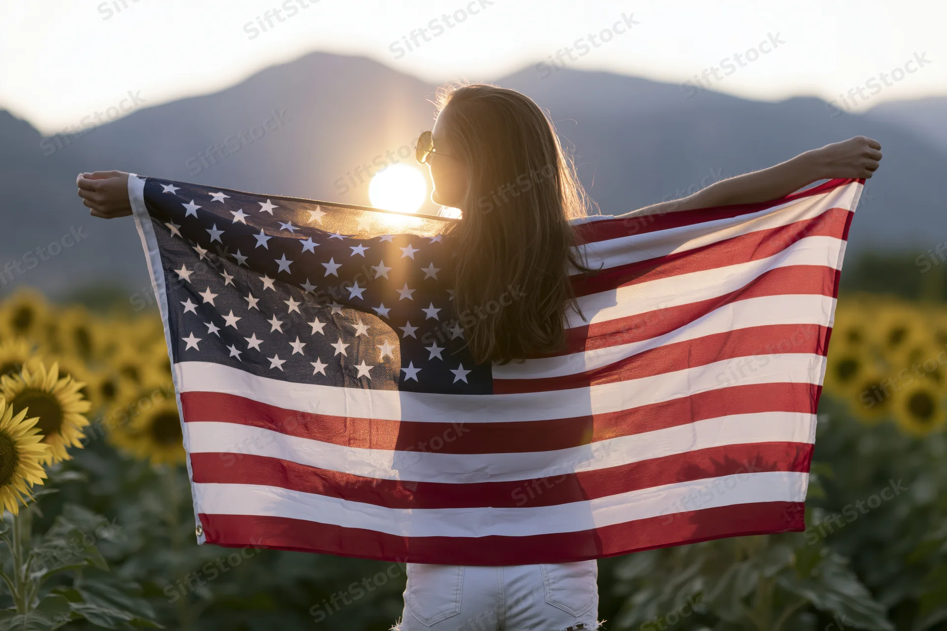 Woman holding american flag spread wide in sunflower field at sunset