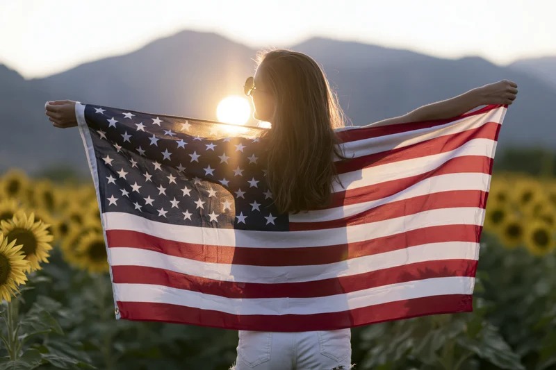 Woman holding american flag spread wide in sunflower field at sunset