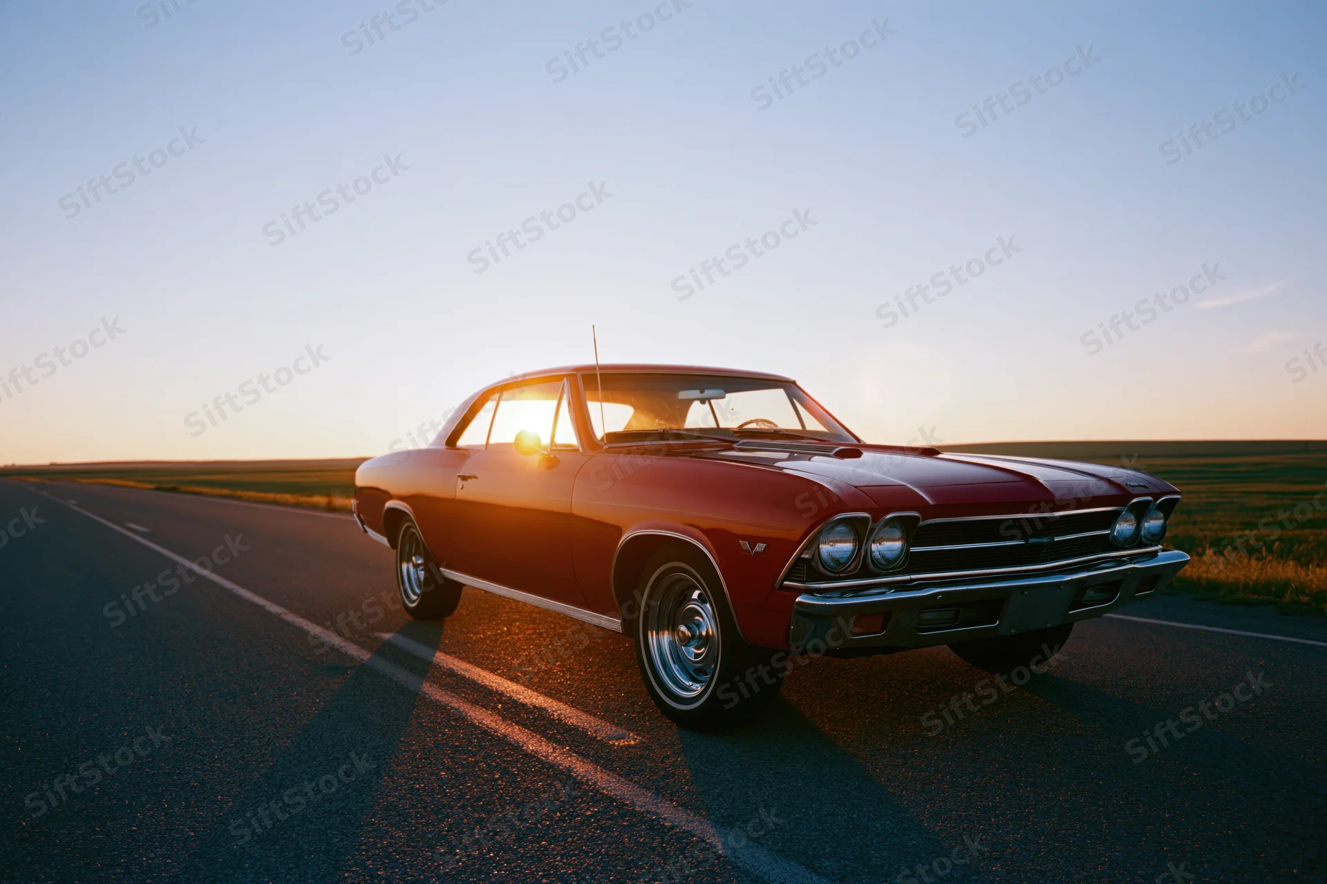 Red 1960s american muscle car parked on two-lane asphalt road at sunset