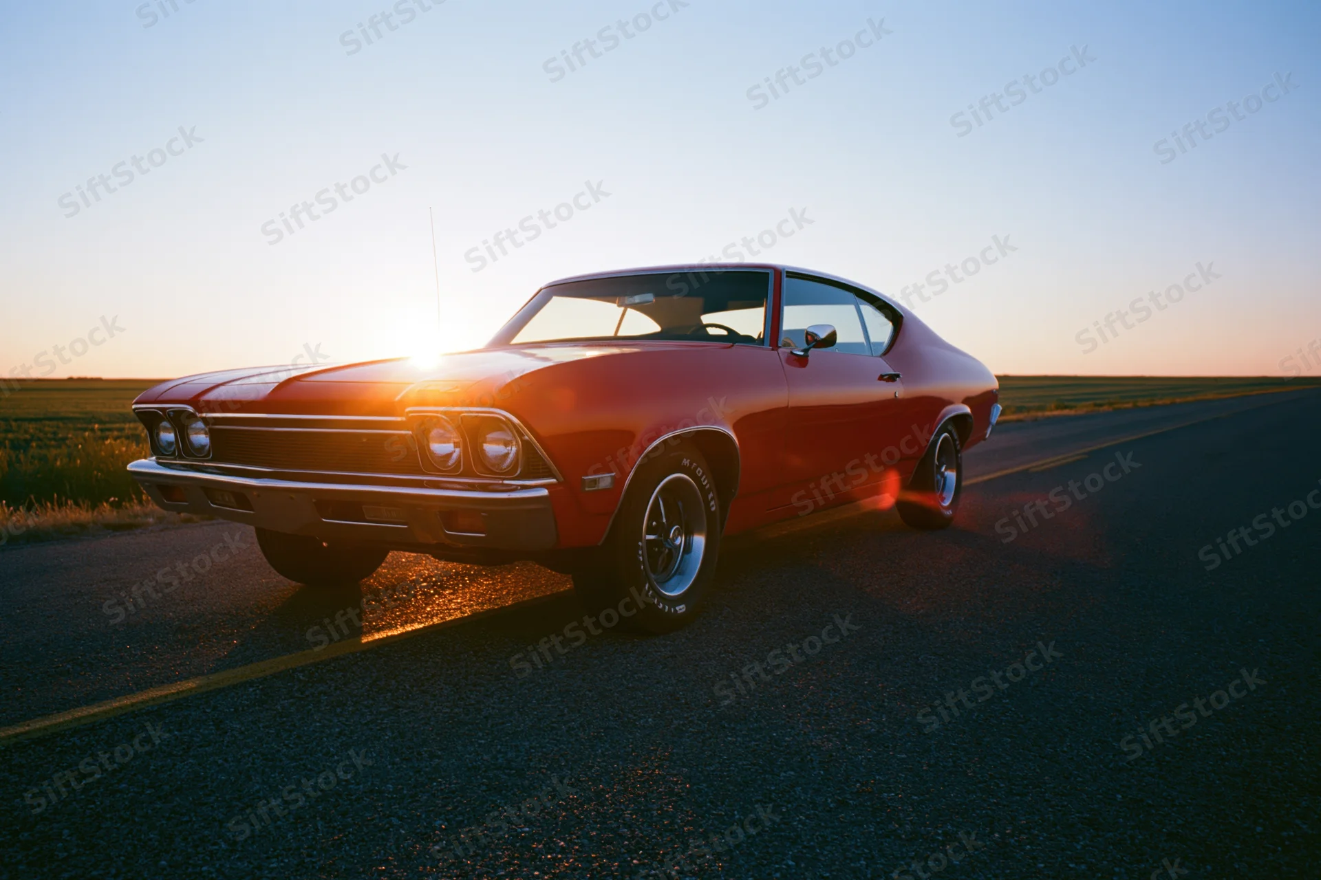 Red 1960s american muscle car parked on two-lane asphalt road at sunset