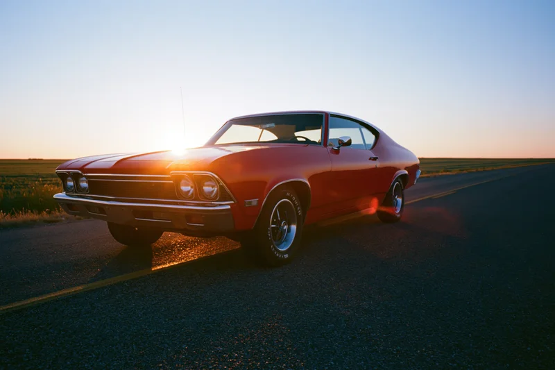 Red 1960s american muscle car parked on two-lane asphalt road at sunset