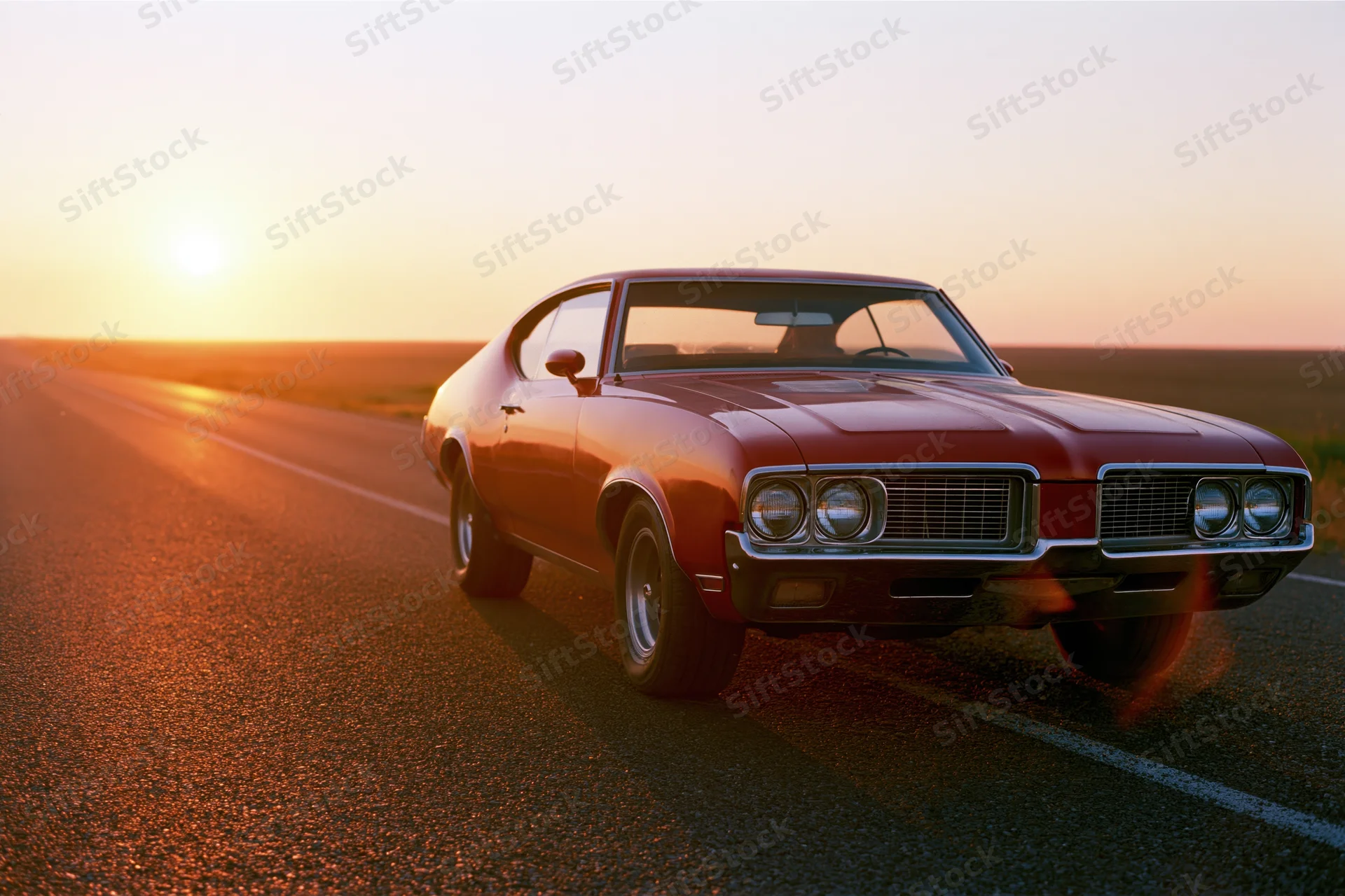 Red 1960s american muscle car parked on empty two-lane highway at sunset
