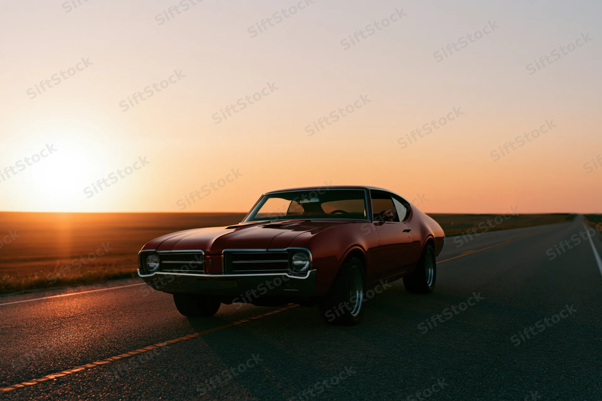Red 1960s american muscle car parked on empty two-lane highway at sunset