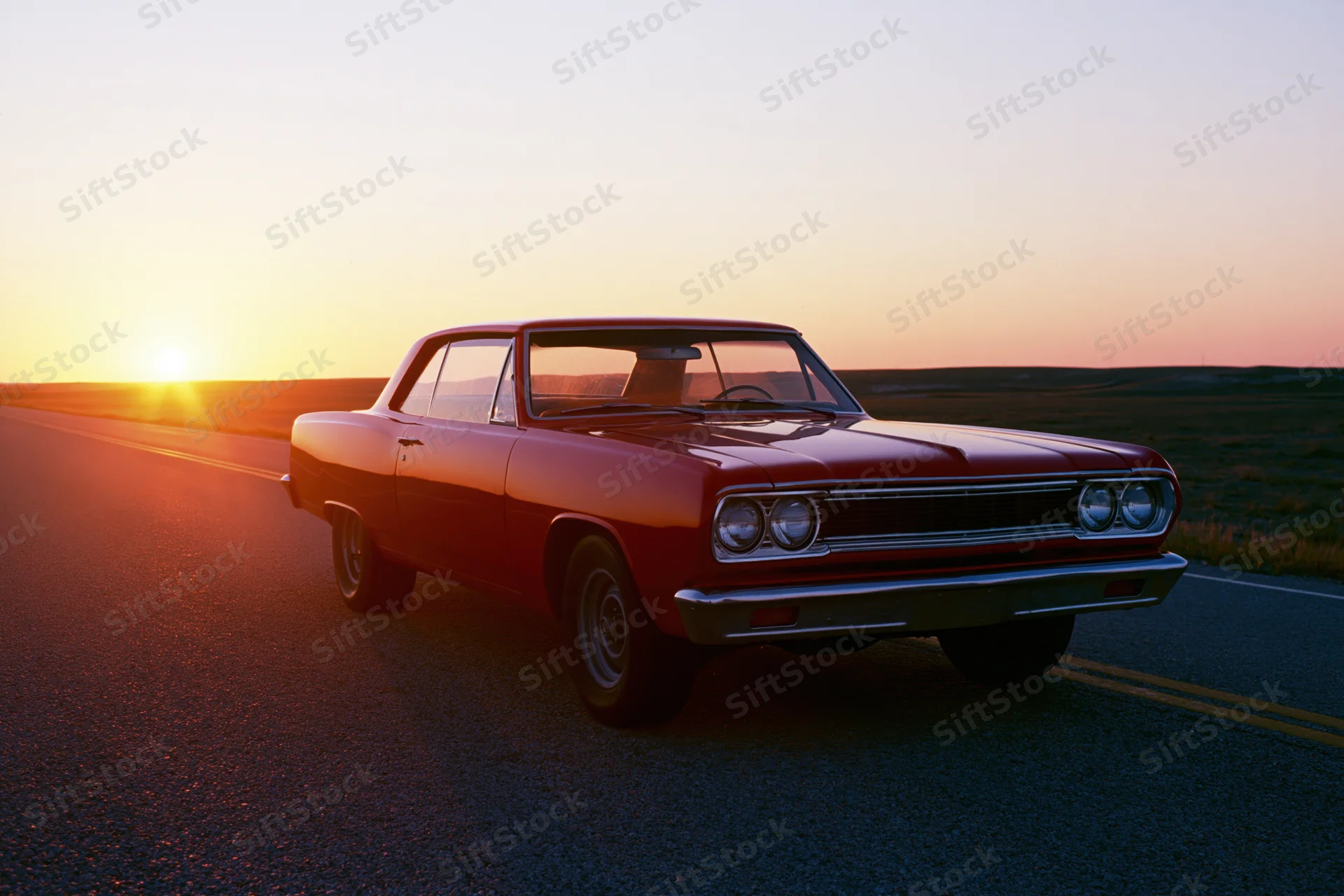 Red 1960s american muscle car parked on empty two-lane highway at sunset