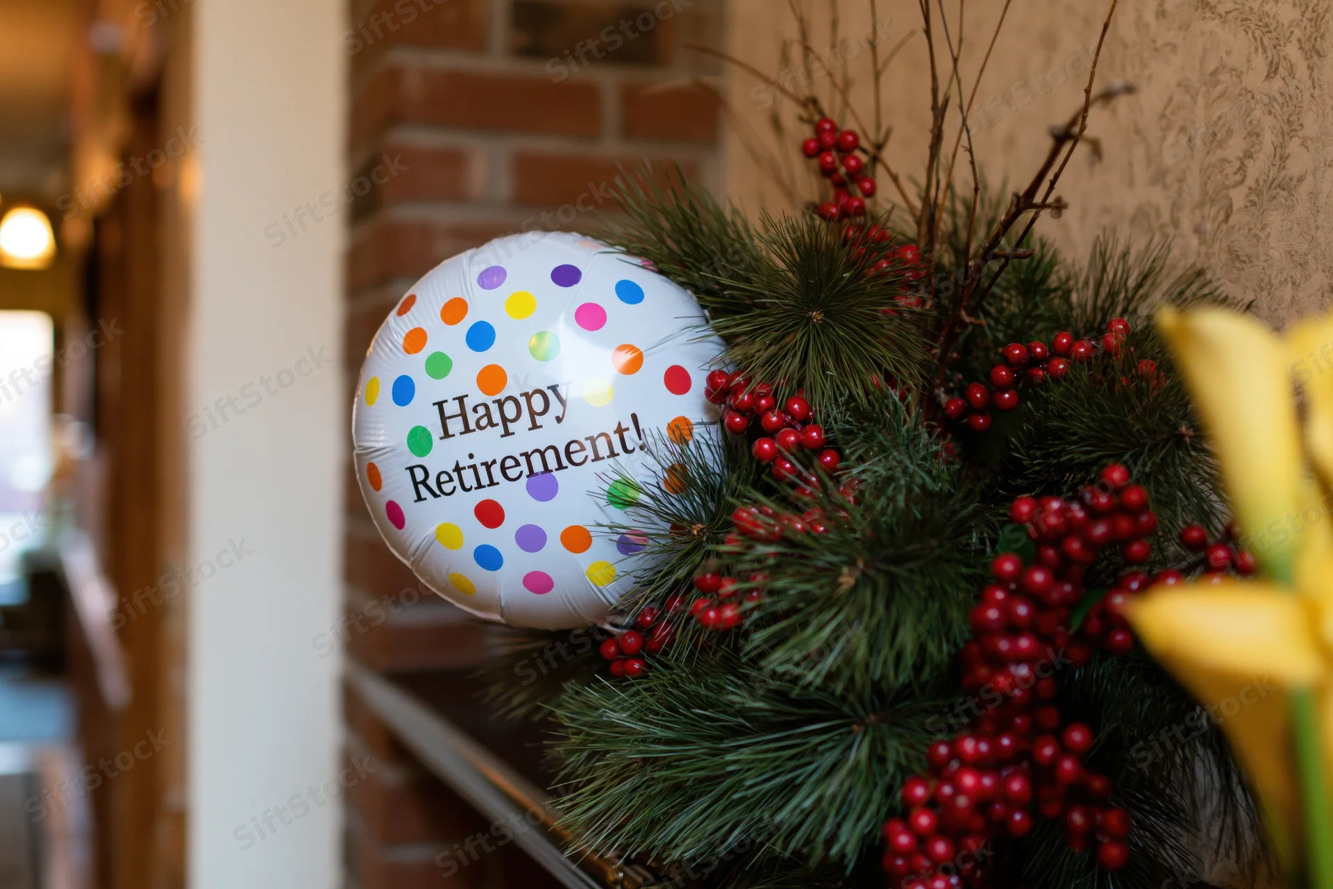 Foil balloon reading happy retirement nestled among pine branches and red berries on a brick shelf indoors
