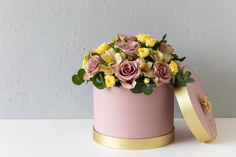 Mixed flower arrangement in a pink and gold hatbox on a white surface