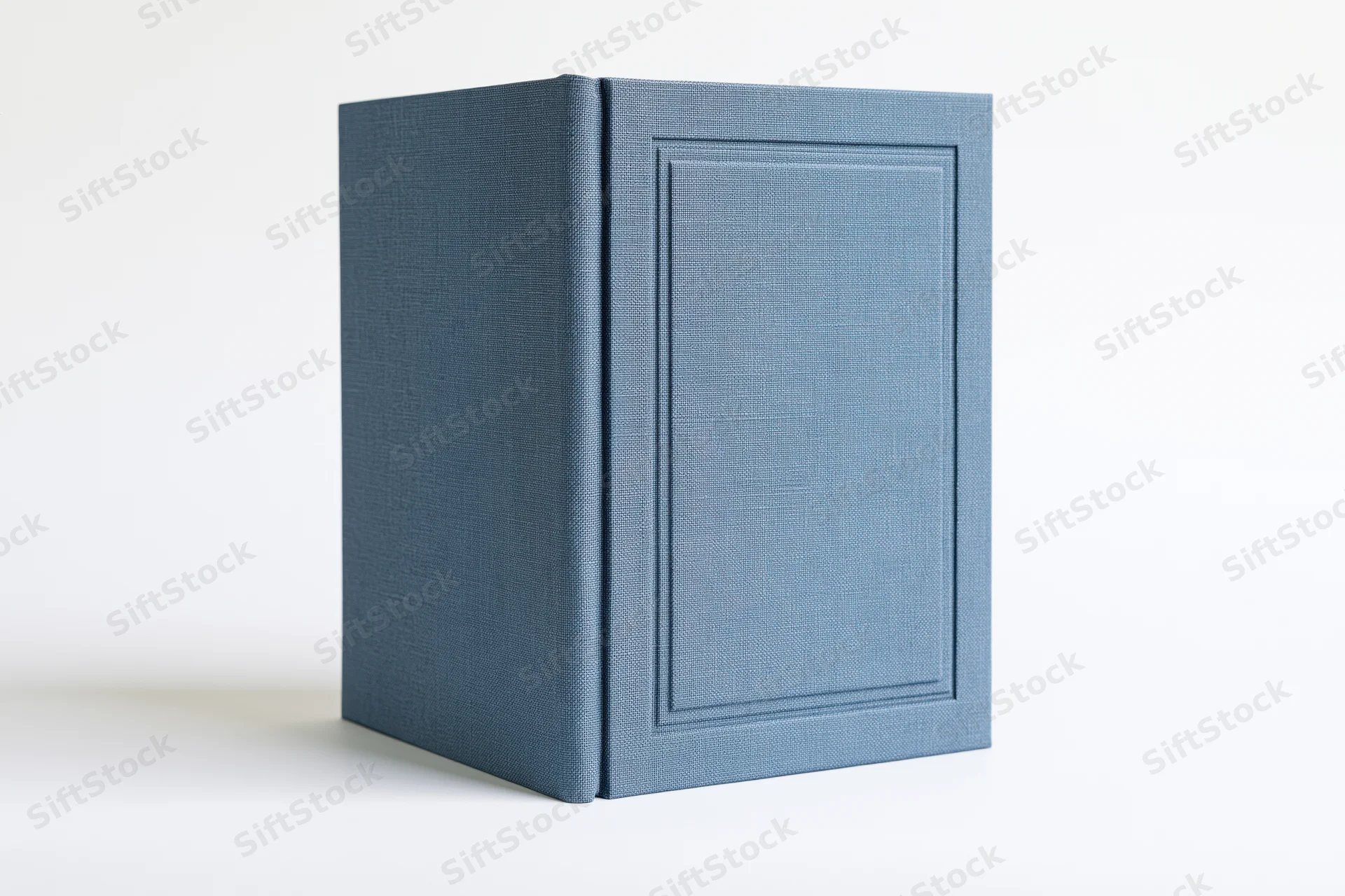 Blank hardcover book with textured blue cloth cover standing upright on white surface