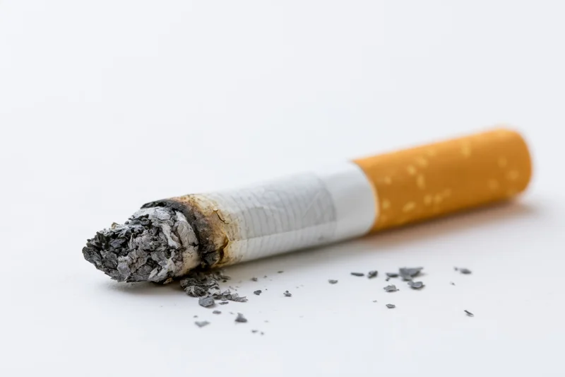 Burnt cigarette butt with ash on white surface