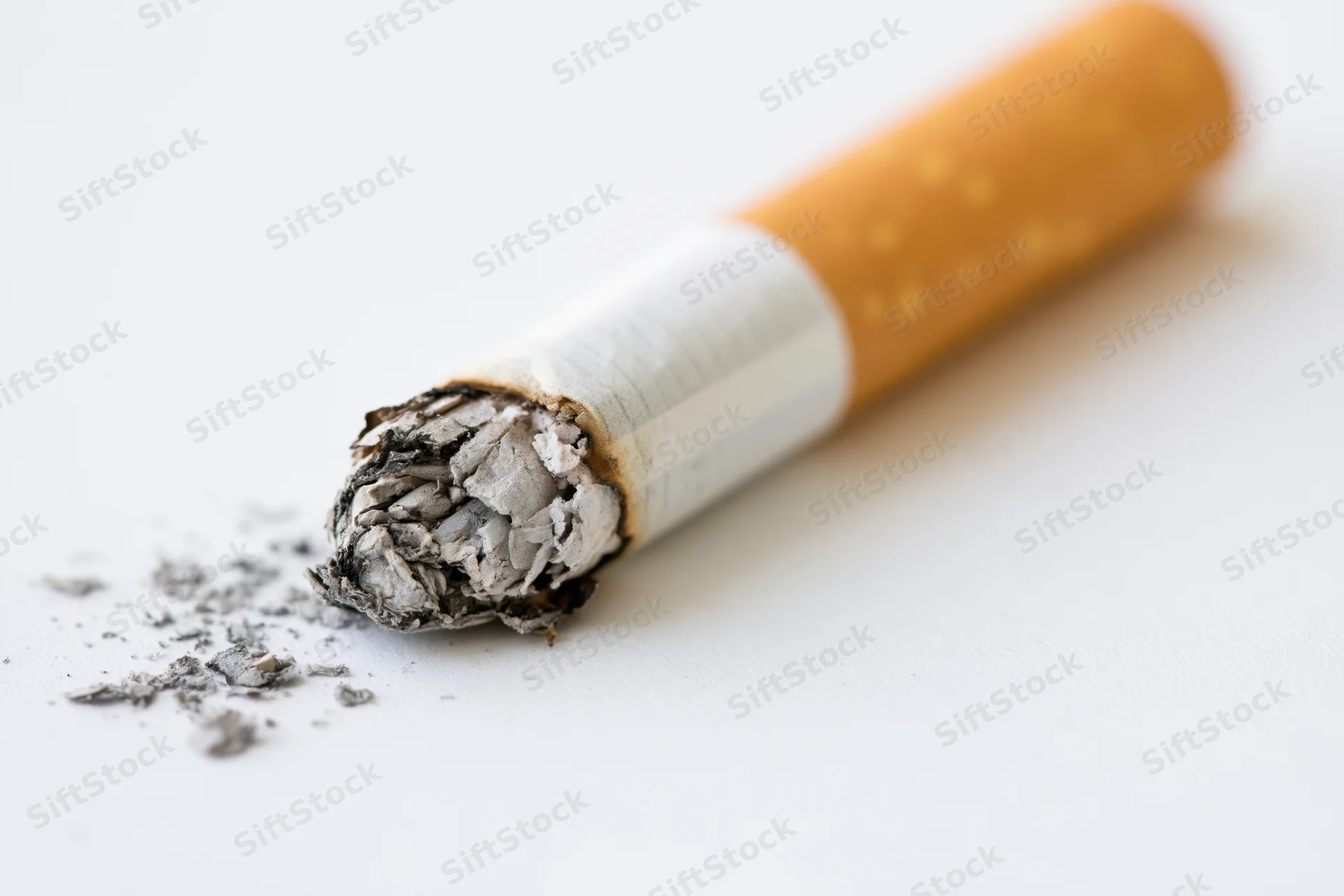 Burnt cigarette butt with ash on white surface
