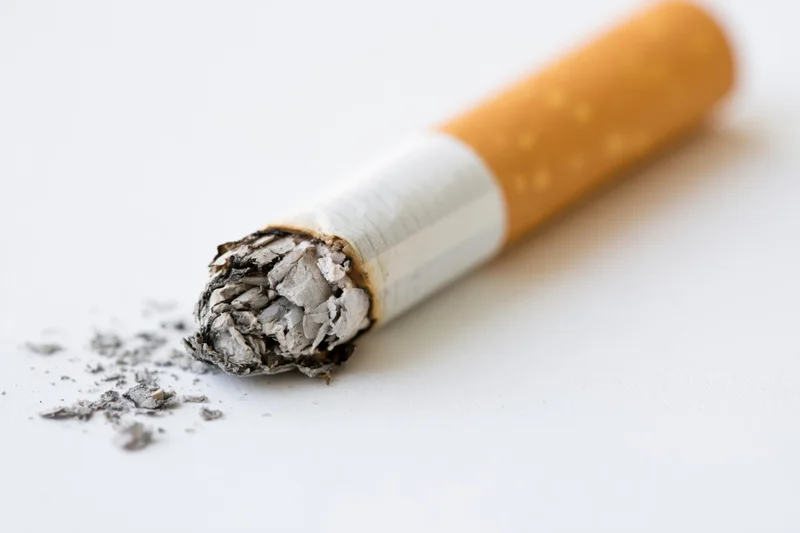 Burnt cigarette butt with ash on white surface