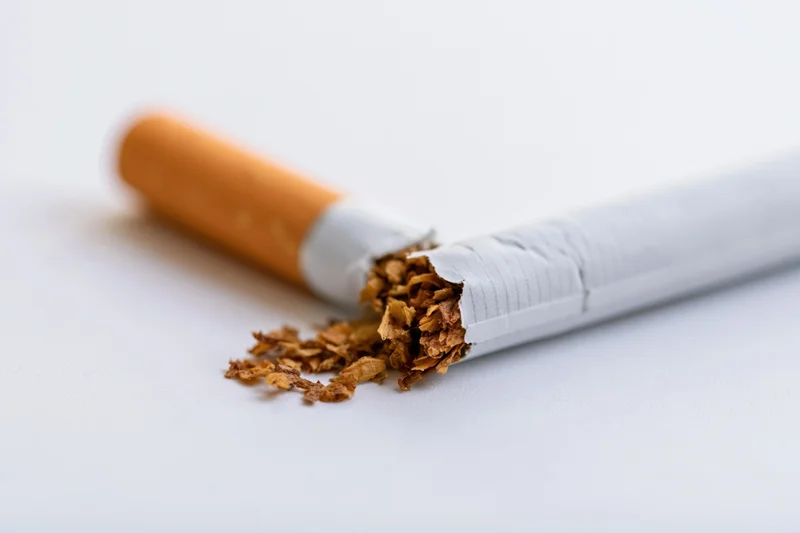 Broken cigarette snapped in half with tobacco spilling out on white surface