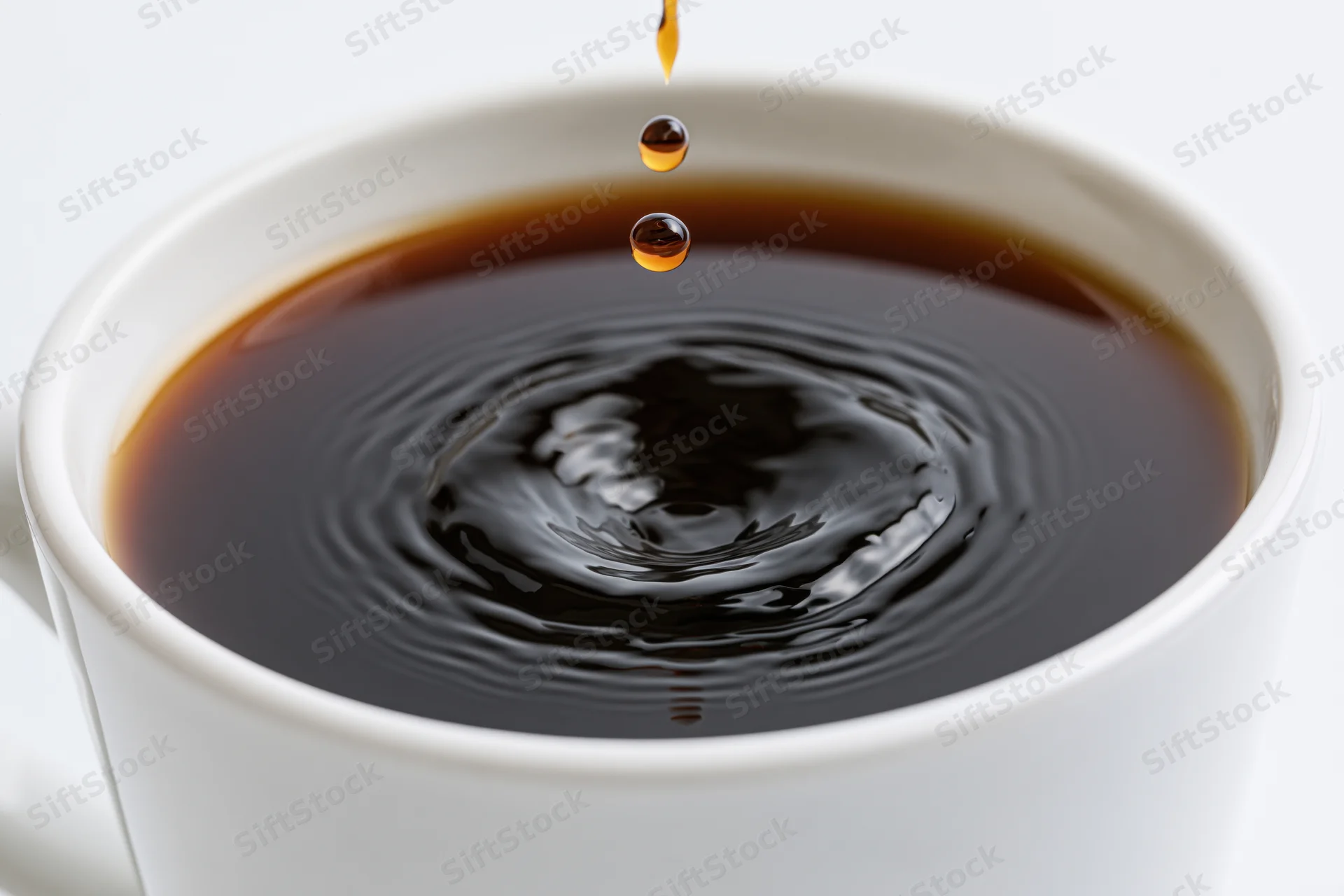 A drop of coffee falling into a white cup, creating ripples on the surface