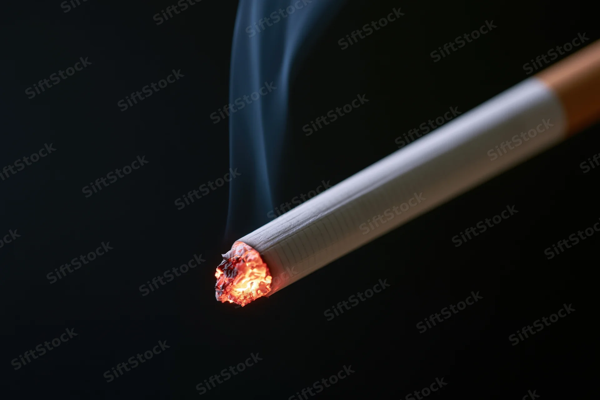 Lit cigarette burning with smoke against black background