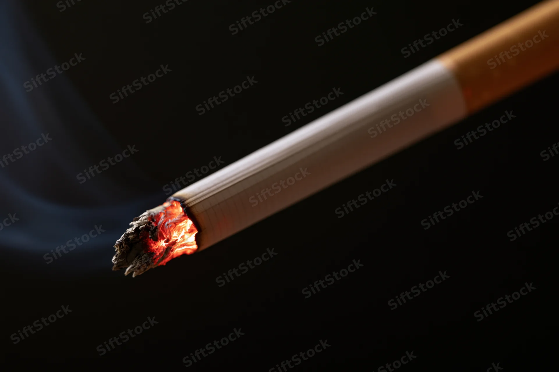 Lit cigarette burning with glowing ember and smoke against black background