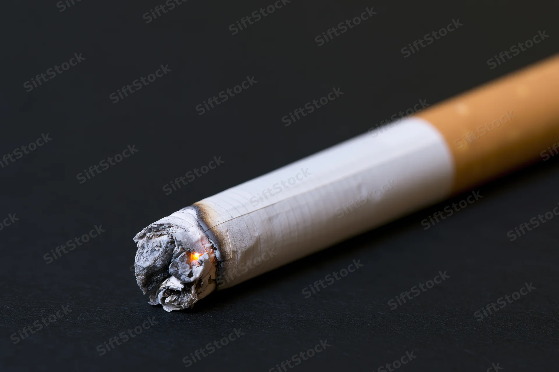 Lit cigarette with burning ember and ash on black surface