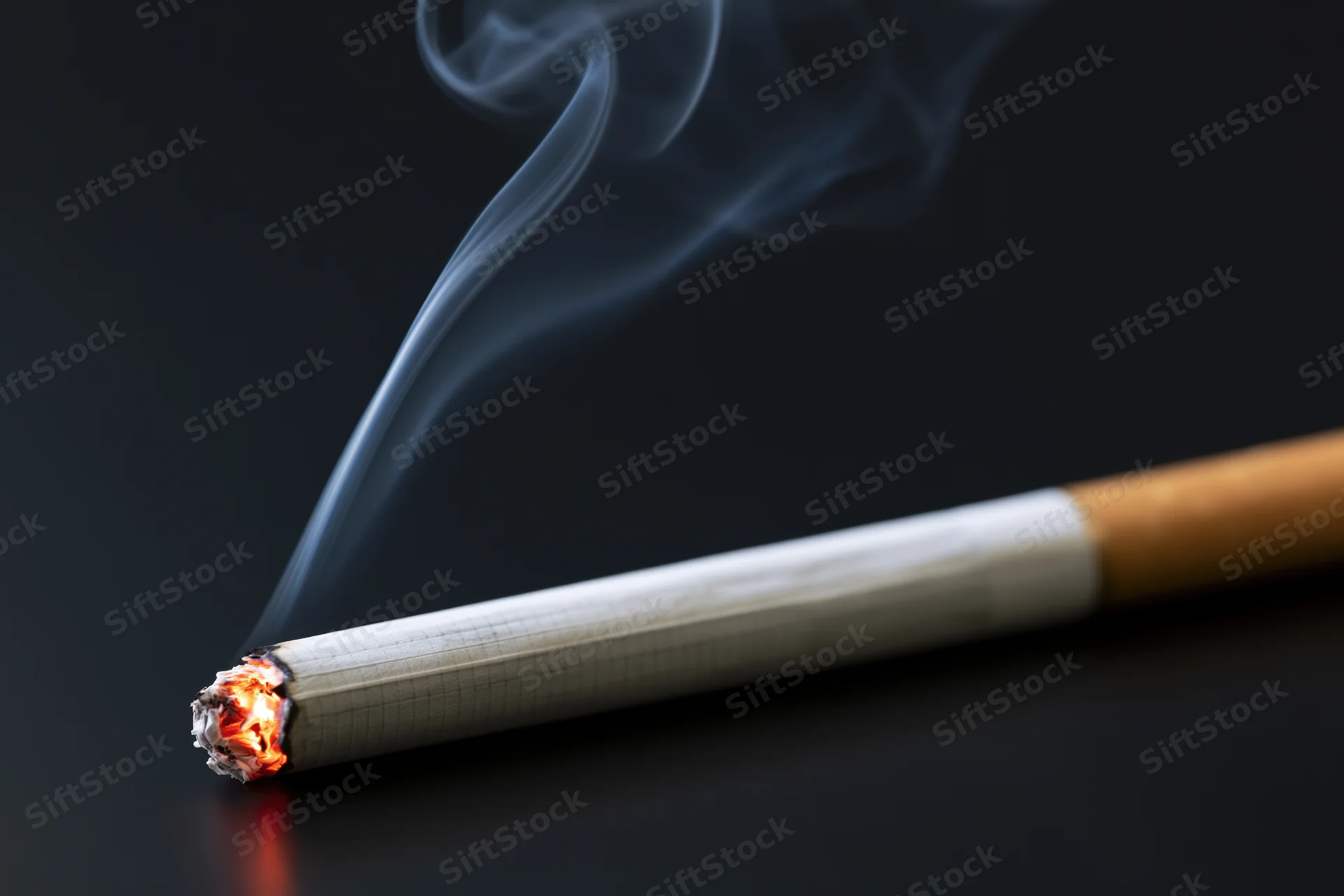 Lit cigarette burning with smoke rising against dark background