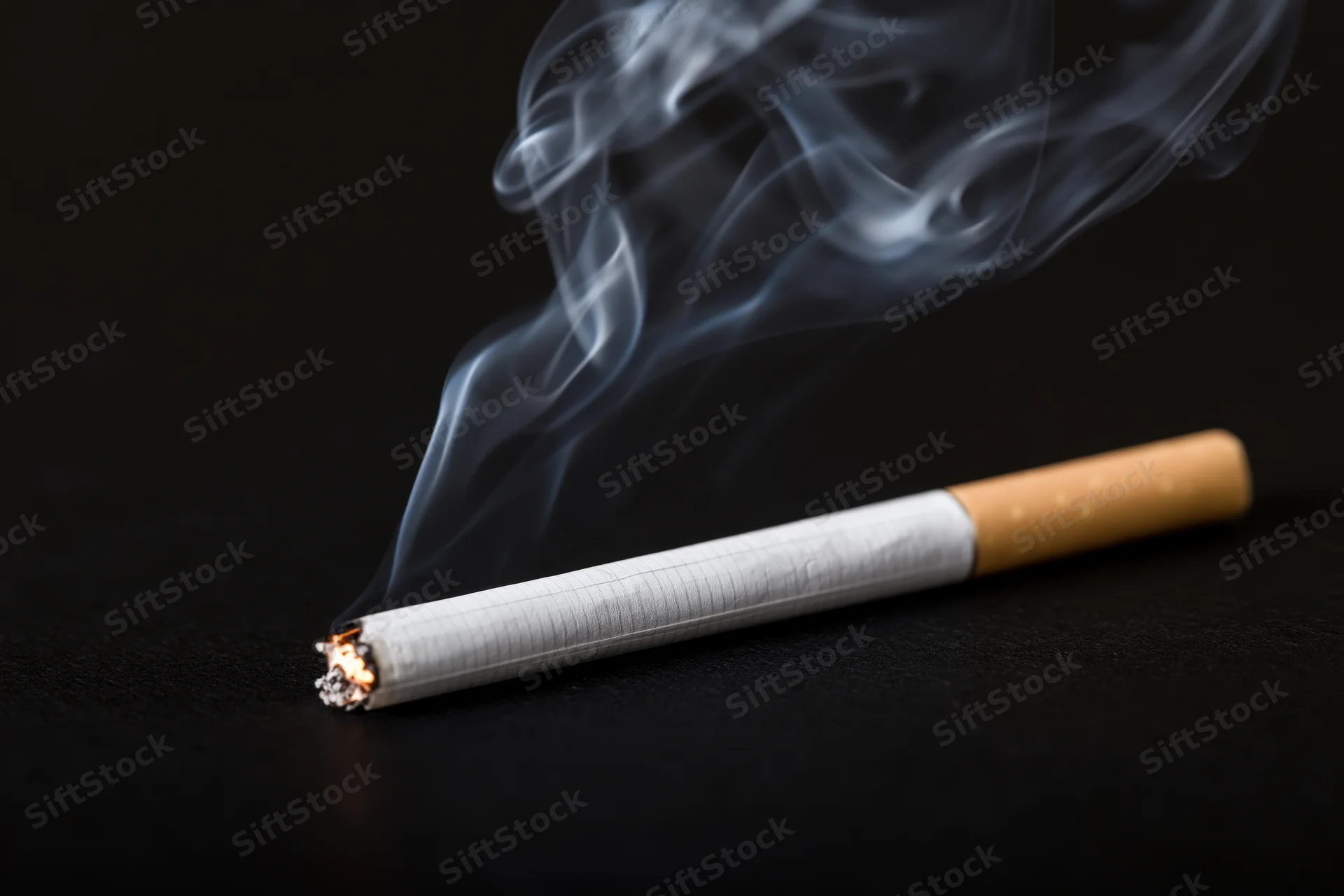 Lit cigarette burning with curling smoke on black surface