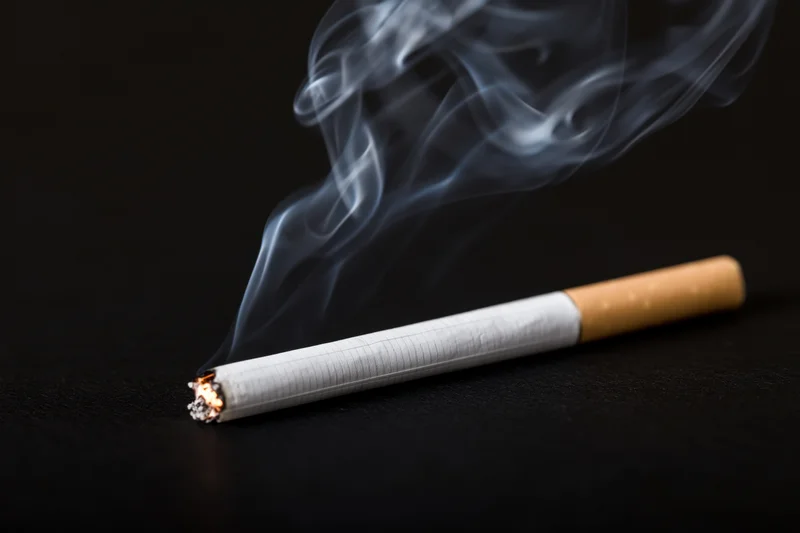Lit cigarette burning with curling smoke on black surface