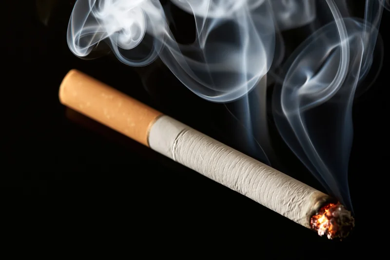 Lit cigarette burning diagonally on black background with curling smoke