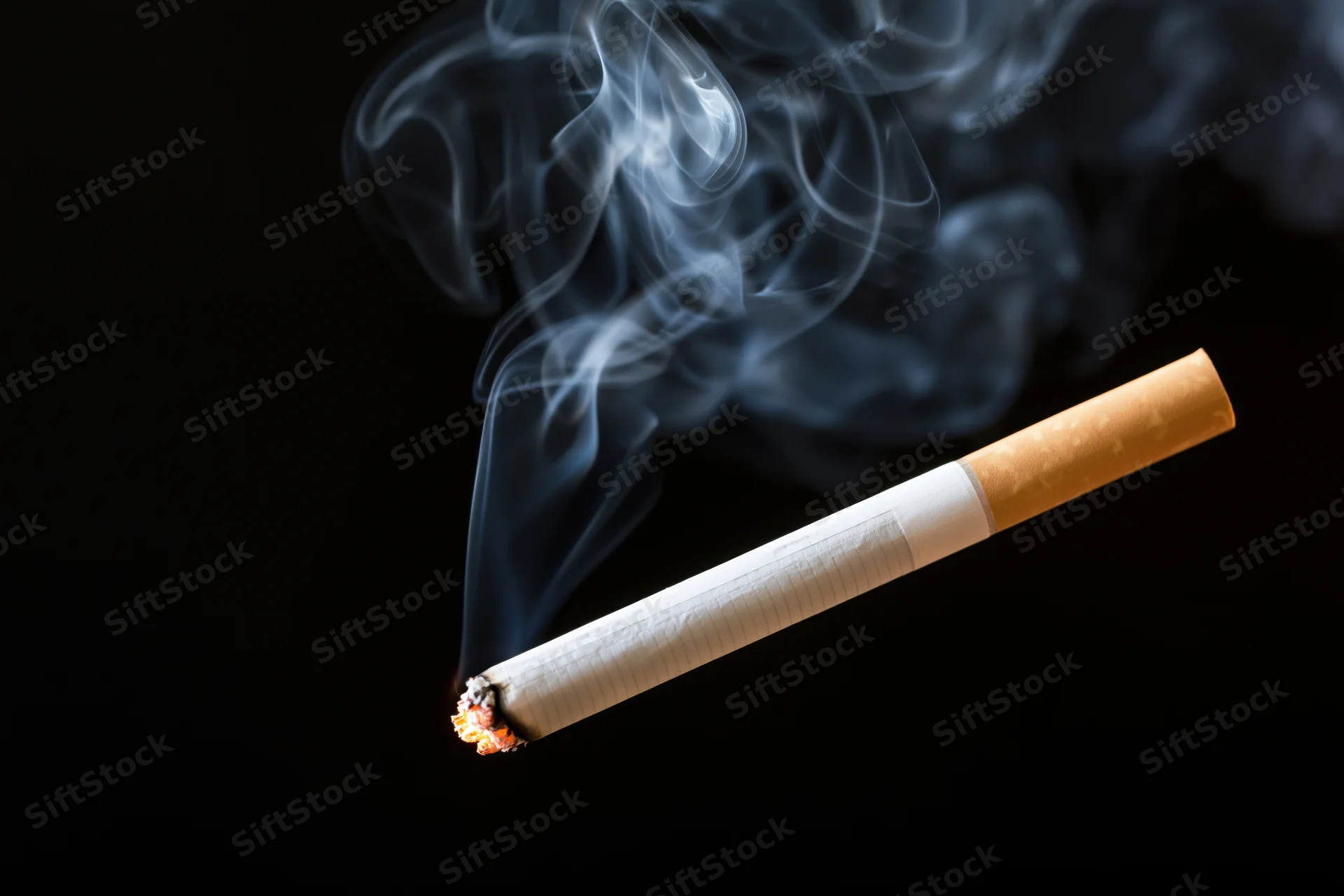 Lit cigarette with curling smoke against black background